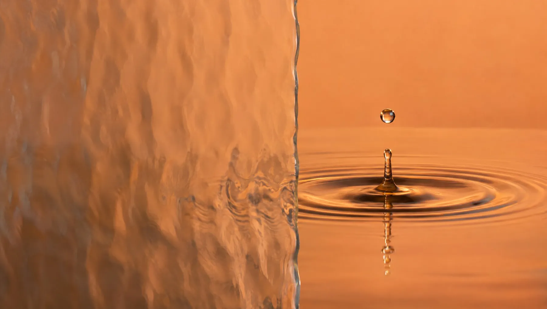 A drop of water landing in still water, half seen through wave glass.